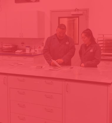 Two lab technicians in RISE Center coats examine material samples.