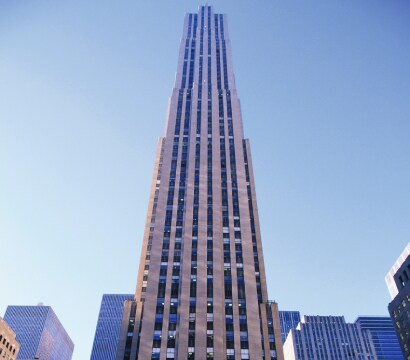 A tall, slender skyscraper with numerous windows reaching towards a clear, light blue sky
