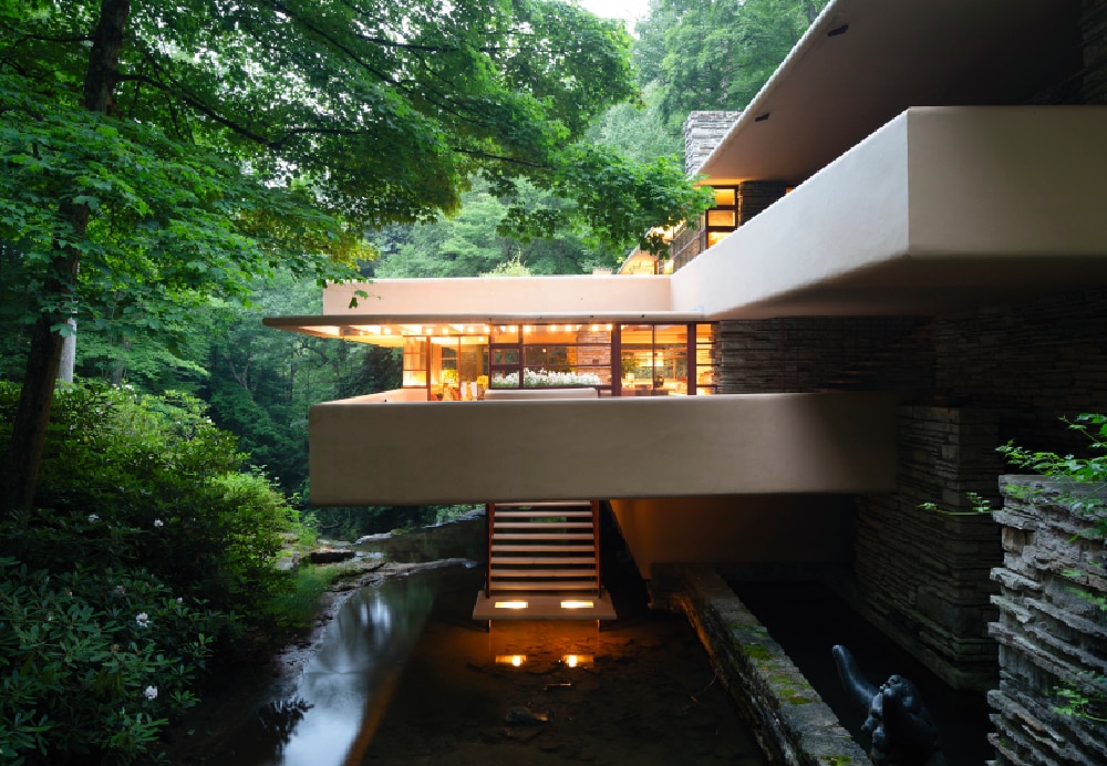 Low-angle view of a concrete balcony suspended over a calm stream, with a suspended staircase leading down to the water's surface.