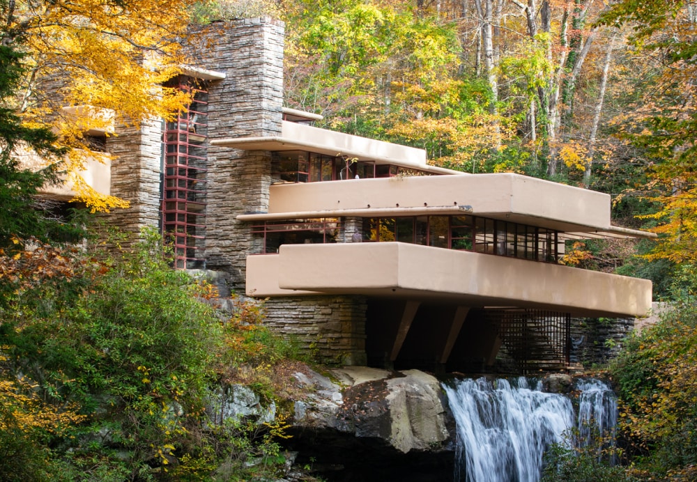 The iconic residence captured during autumn, framed by vibrant yellow and orange trees with a waterfall flowing beneath the main structure.