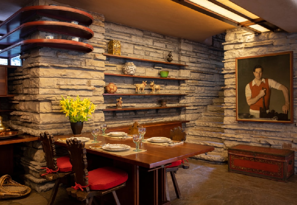 Interior dining area featuring a wooden table with red cushioned chairs, set against rough-cut stone walls and built-in shelving.