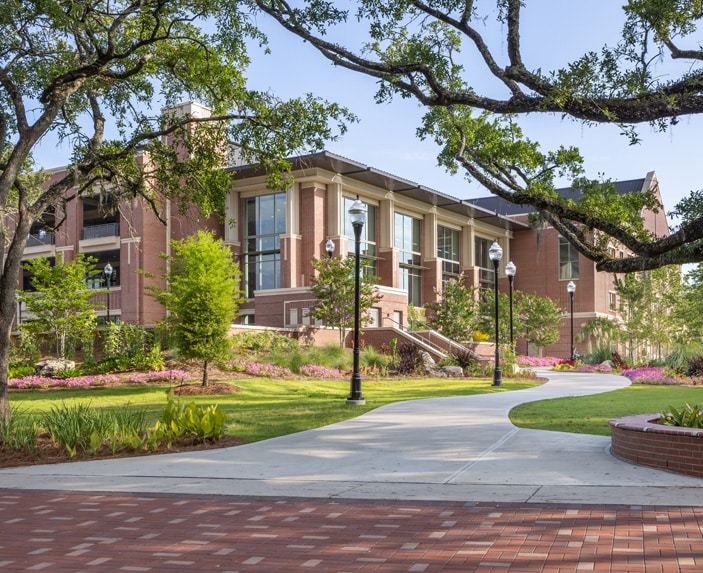 The Student Union building at Florida State University with large windows is surrounded by trees, landscaped gardens, and a curved sidewalk on a sunny day.