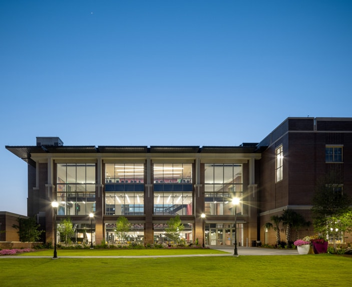 The Student Union building at Florida State University with large glass windows is illuminated at dusk. The well-manicured lawn and pathway lead to the entrance, creating a welcoming vibe.