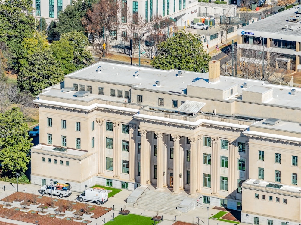 Aerial view of a Neoclassical government building featuring a prominent white flat roof and a grand columned entrance.