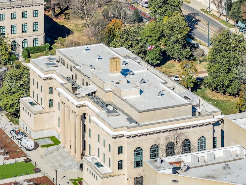 High-angle perspective of a limestone civic building with arched windows and a central flag pole flying the American flag.