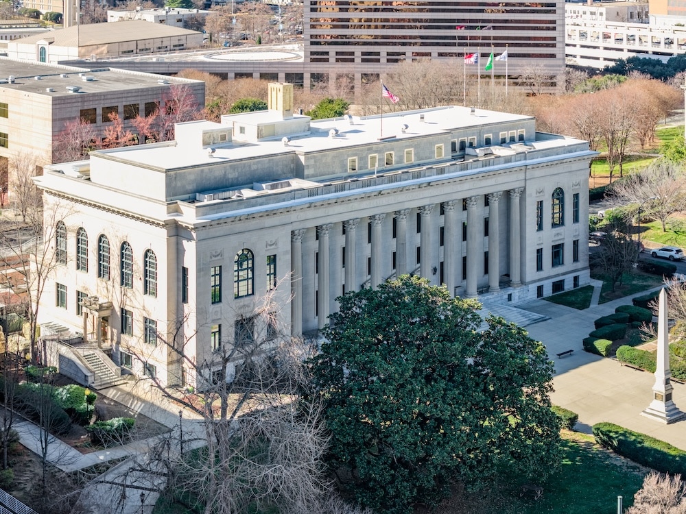 Side-angle view of a historic courthouse architecture showcasing a row of tall Corinthian columns and lush green landscaping.