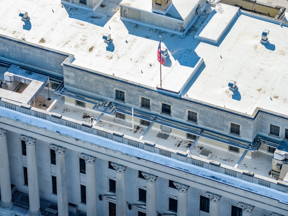 Close-up of a building's upper facade showing the engraved stone lettering above a colonnade and industrial rooftop piping.