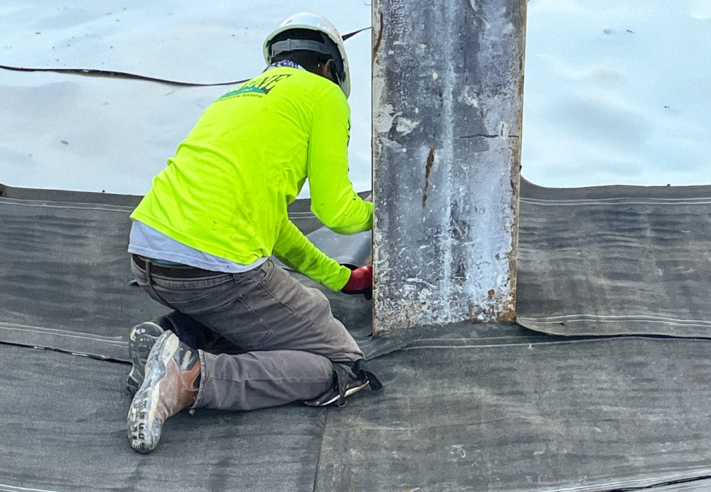 Construction professional installing a thick waterproof membrane around a vertical steel support beam during the foundation phase of a luxury high-rise.