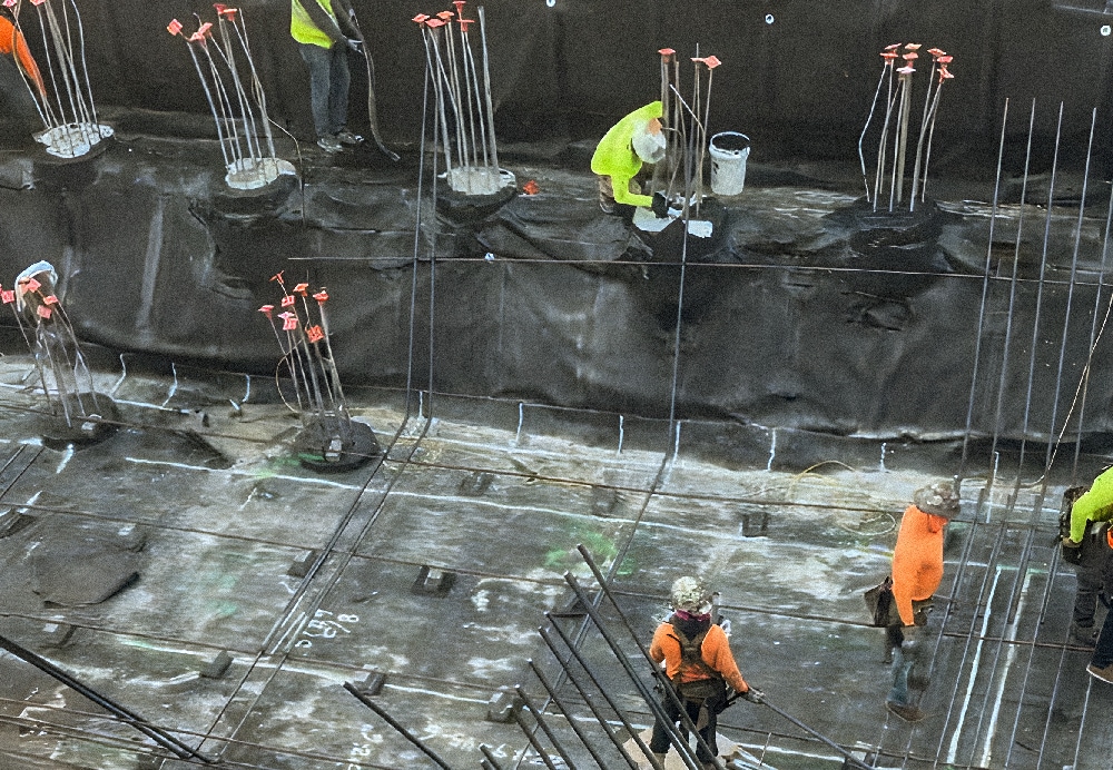 Construction crew securing vertical rebar pile caps and waterproofing layers within a large-scale building footprint in Bal Harbour.