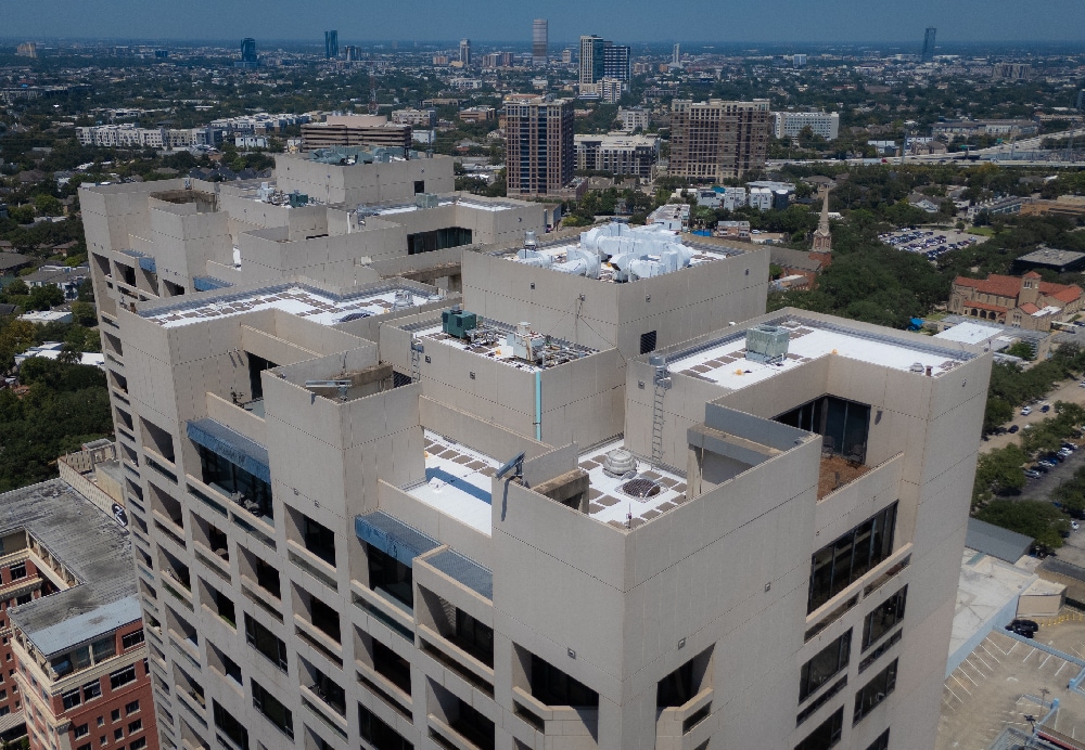 Aerial perspective of a luxury high-rise rooftop featuring modern HVAC systems and white roofing in Houston.
