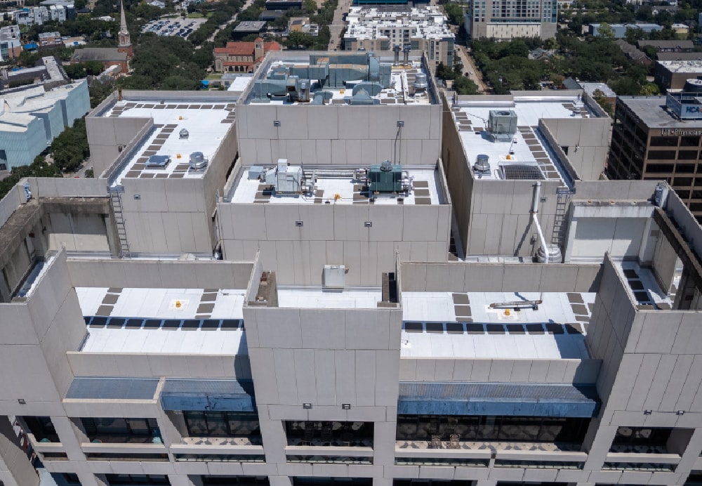 Top-down drone view of a multi-level skyscraper roof with mechanical equipment and industrial ventilation units.