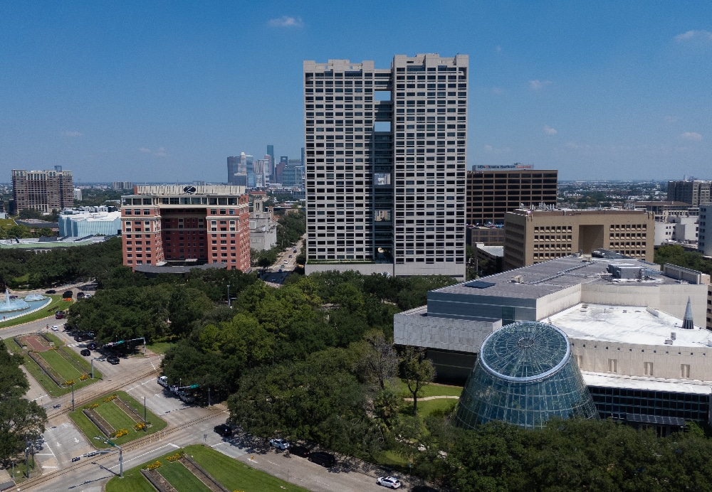 Wide architectural shot of a tall apartment building adjacent to a glass dome museum and manicured urban green space.