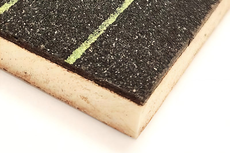 Close-up of high-density foam insulation core with a textured black bitumen surfacing and green markings.
