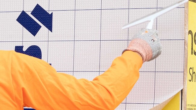 Worker using a squeegee to smooth out a self-adhered air barrier membrane on a wall.