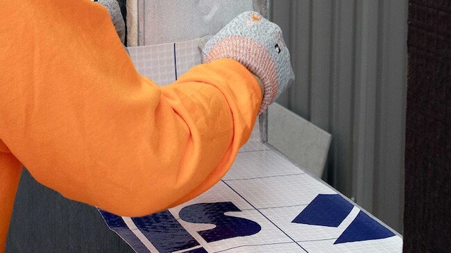 Worker detailing a window sill using self-adhered flashing for water-resistive protection.