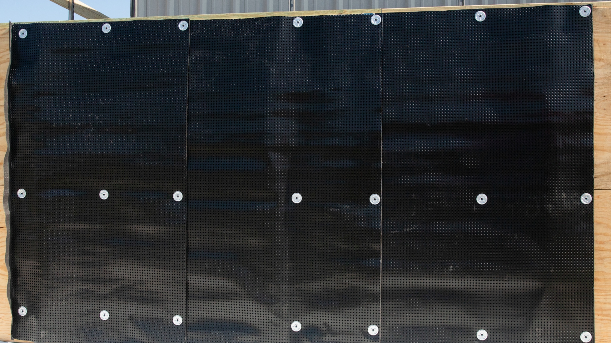 Close-up of a black dimpled drainage mat mechanically fastened to a wall, showing proper installation of the composite.