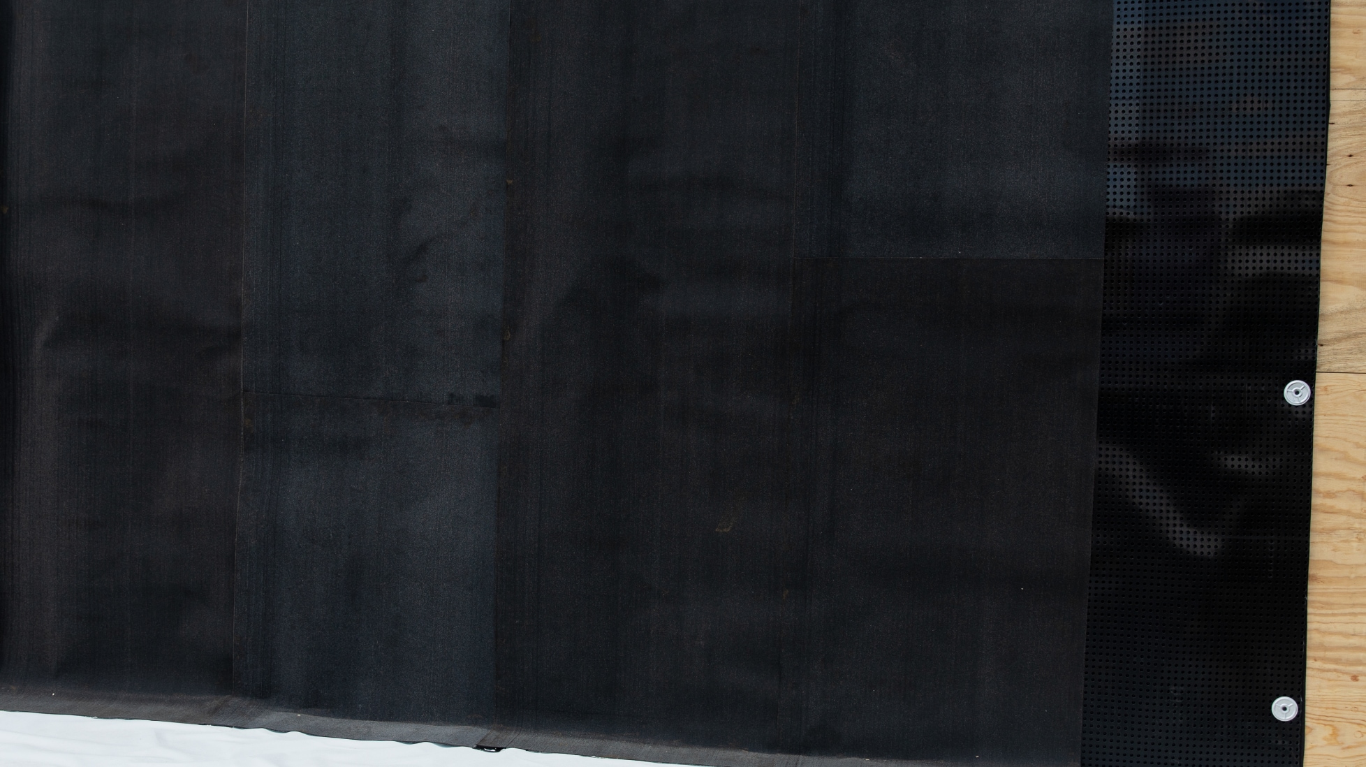 Close-up of a black, fabric-faced waterproofing membrane installed on a vertical wall.