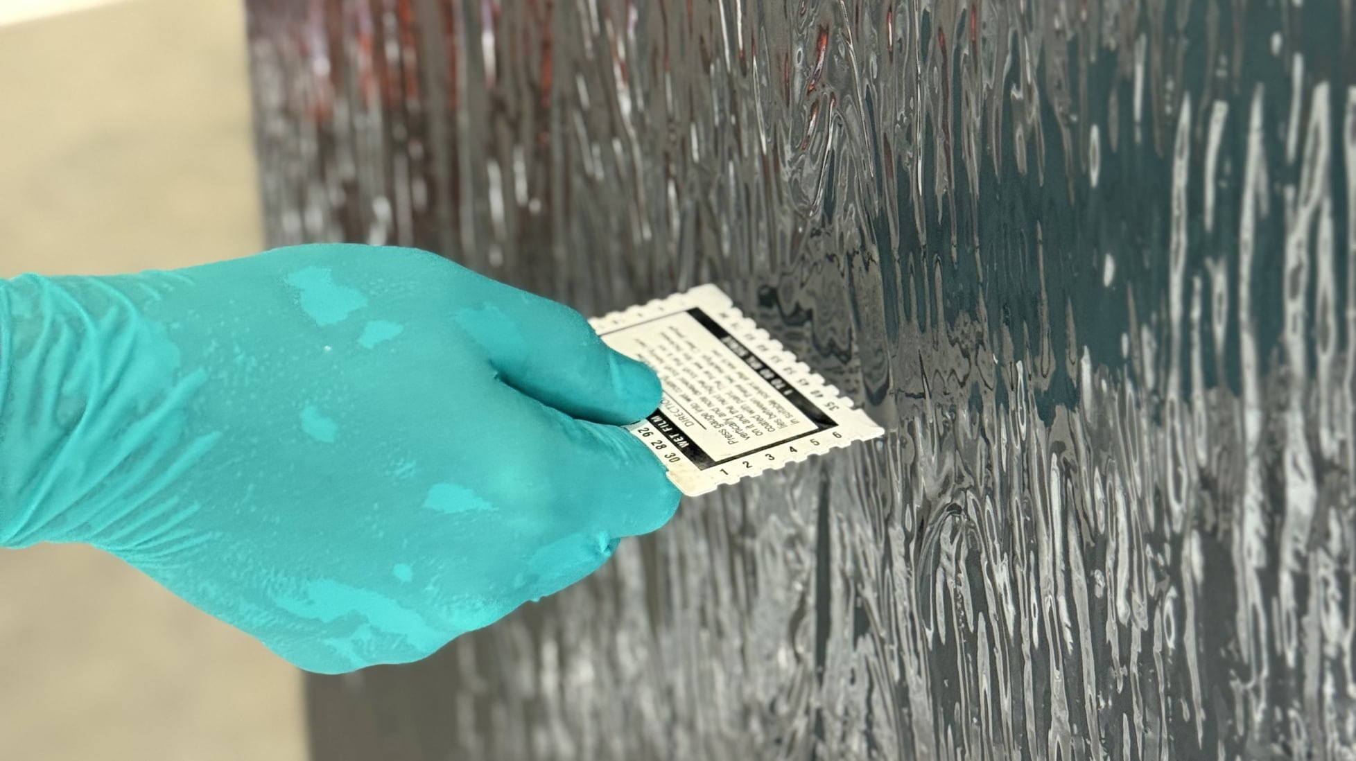 A gloved hand uses a tool to apply the liquid TeraPROOF™ STP Membrane to a vertical surface
