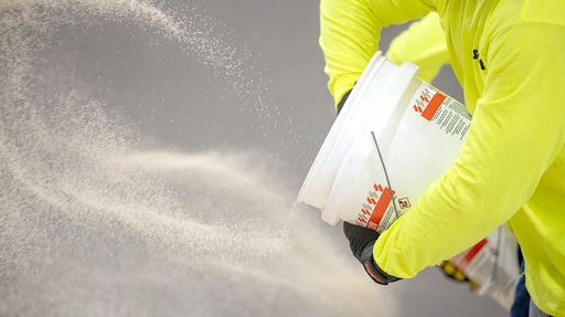 Man in yellow coveralls spreading pro natural quartz from a bucket