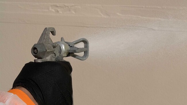 Close-up of a worker using a high-pressure spray gun to apply liquid air and water-resistive barrier.