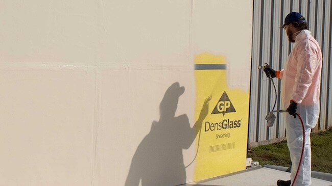 Worker spraying Siplast WALLcontrol over DensGlass sheathing for a commercial wall system.