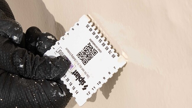 Contractor using a wet film thickness gauge to measure the application depth of a liquid barrier.
