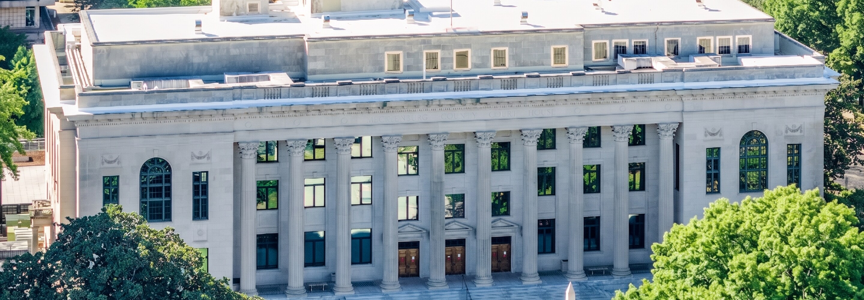 Aerial view of a Neoclassical government building featuring a prominent white flat roof and a grand columned entrance.