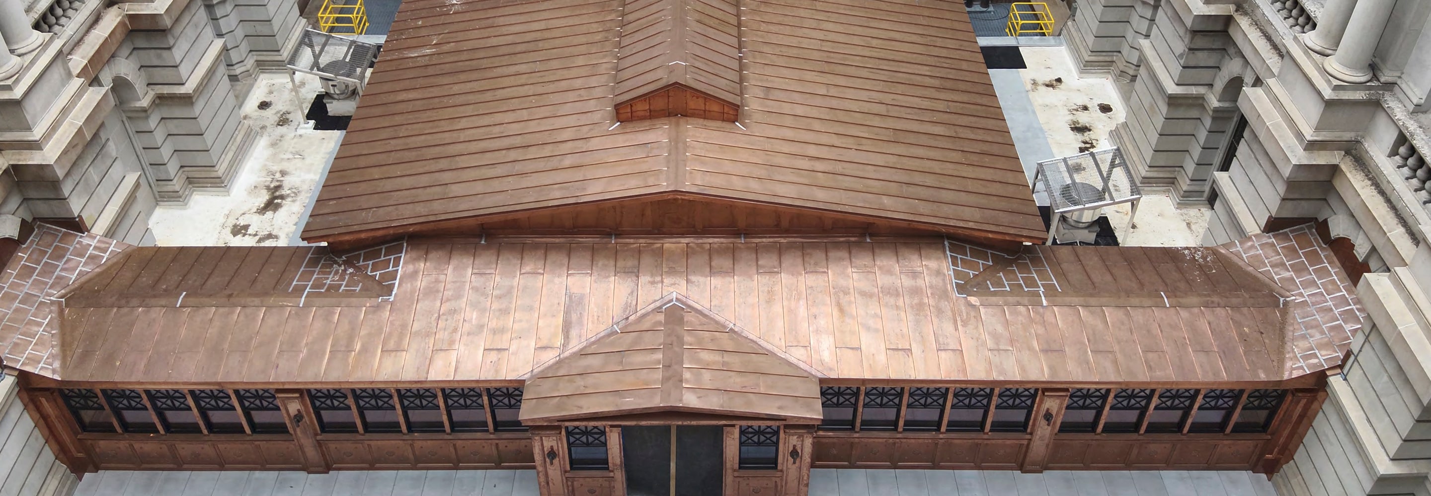 Wide overhead view of a detailed copper roofing installation on a historic building conservatory, surrounded by classical stone masonry facades and rooftop walkways.