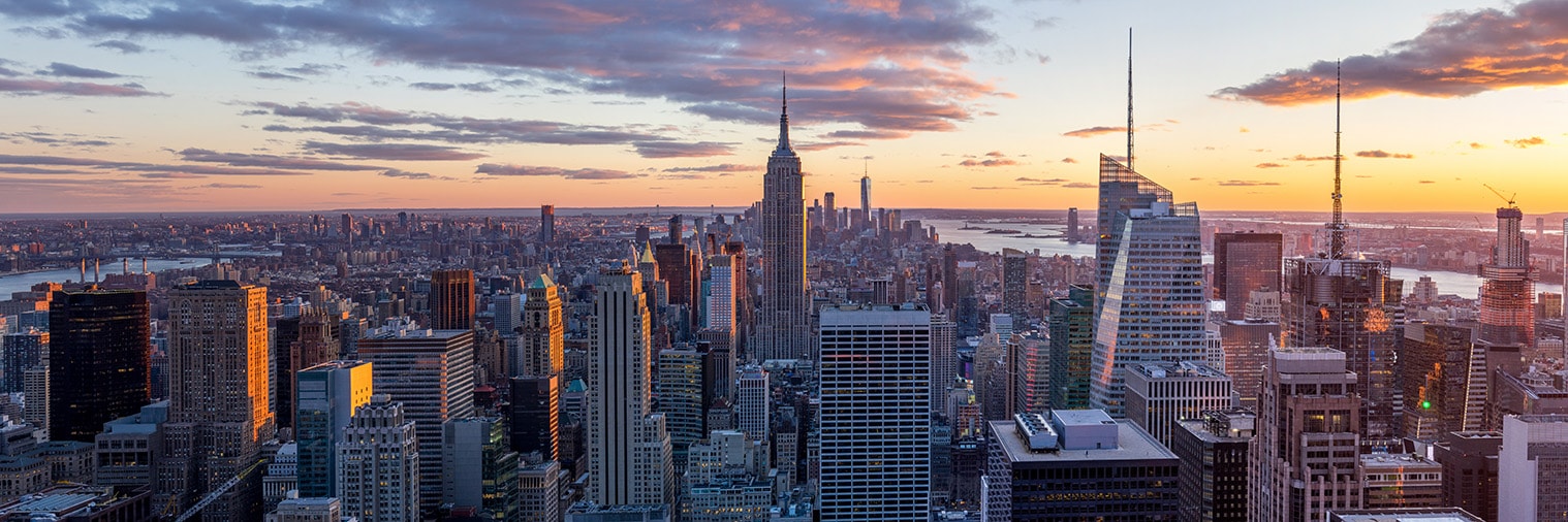 Panoramic view of the New York City skyline at sunset, featuring the Empire State Building and other skyscrapers.