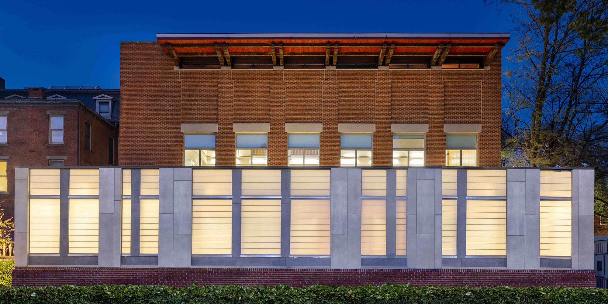 The Joseph Slifka Center for for Jewish Life at Yale, with a modern building facade featuring a lighted wall with horizontal panels, contrasting with a brick structure under a twilight sky.