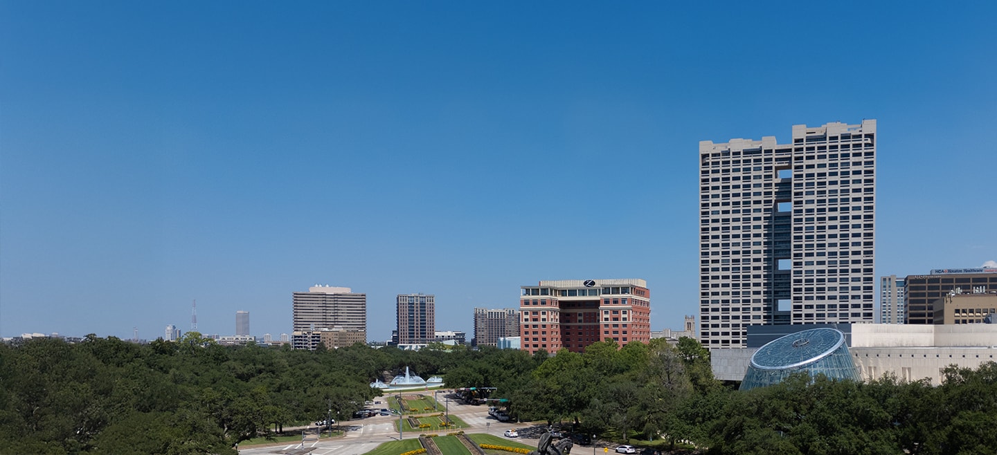 The Warwick Towers luxury high-rise building in Houston, viewed from a distance across a park with other Museum District skyline buildings.