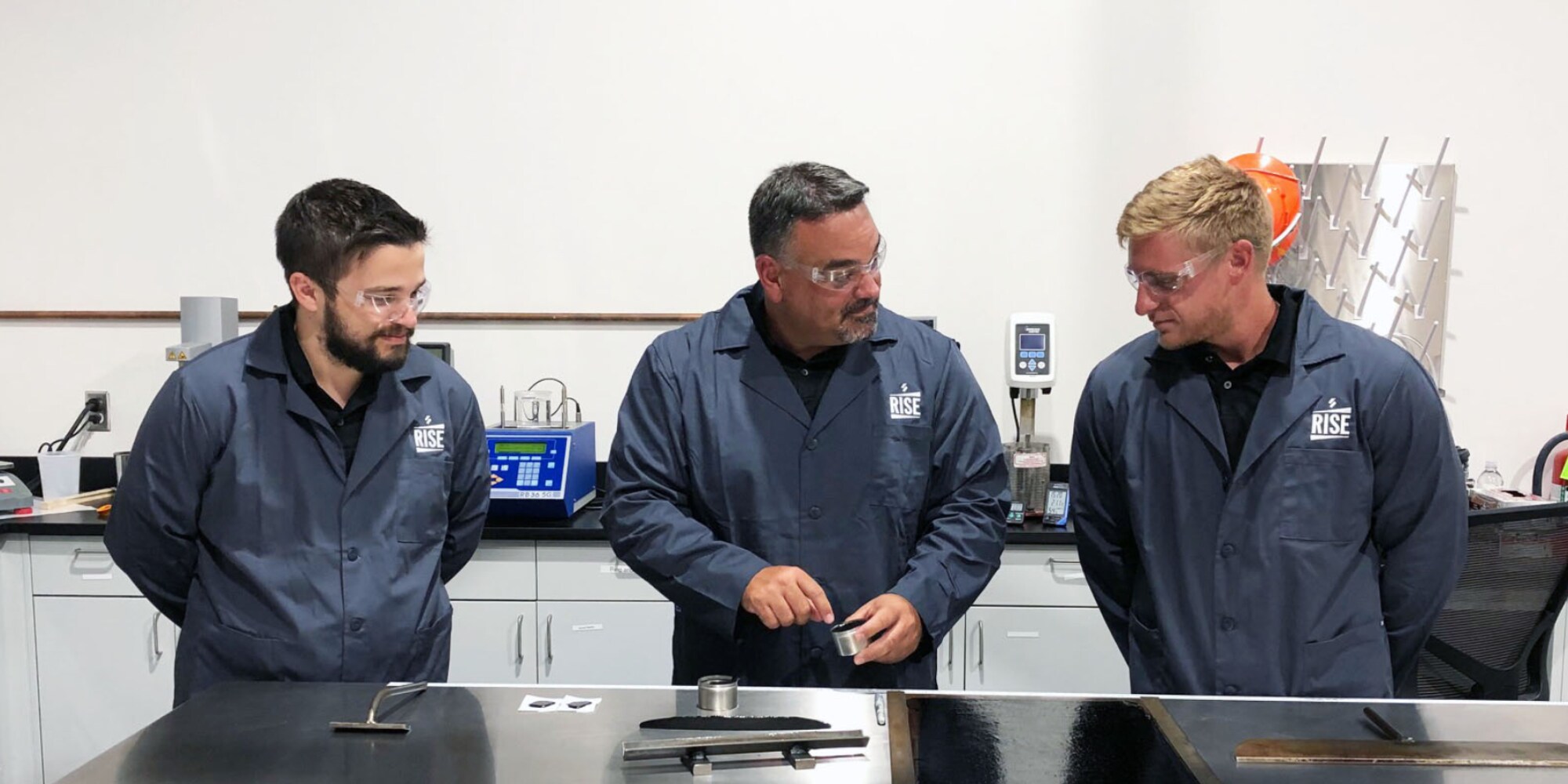Three lab technicians in RISE Center coats inspecting a sample, representing Siplast's advanced roofing and waterproofing solutions.