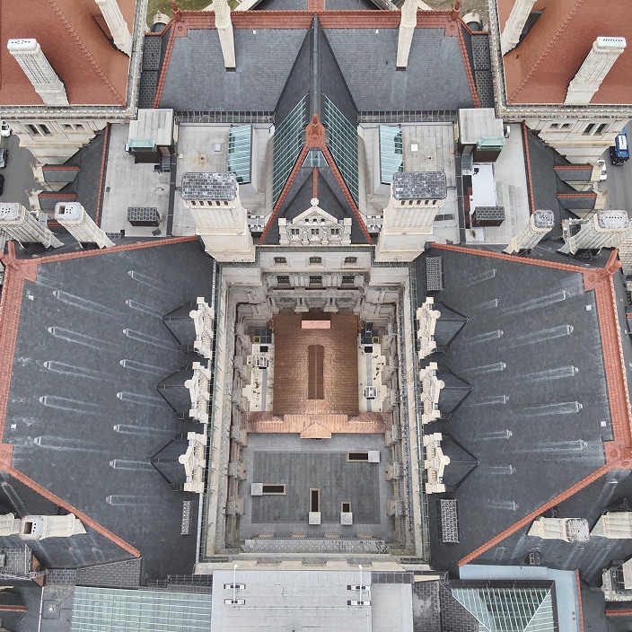 Aerial top-down view of an ornate historic building featuring dark slate roofing, terracotta tile accents, and a central inner courtyard.