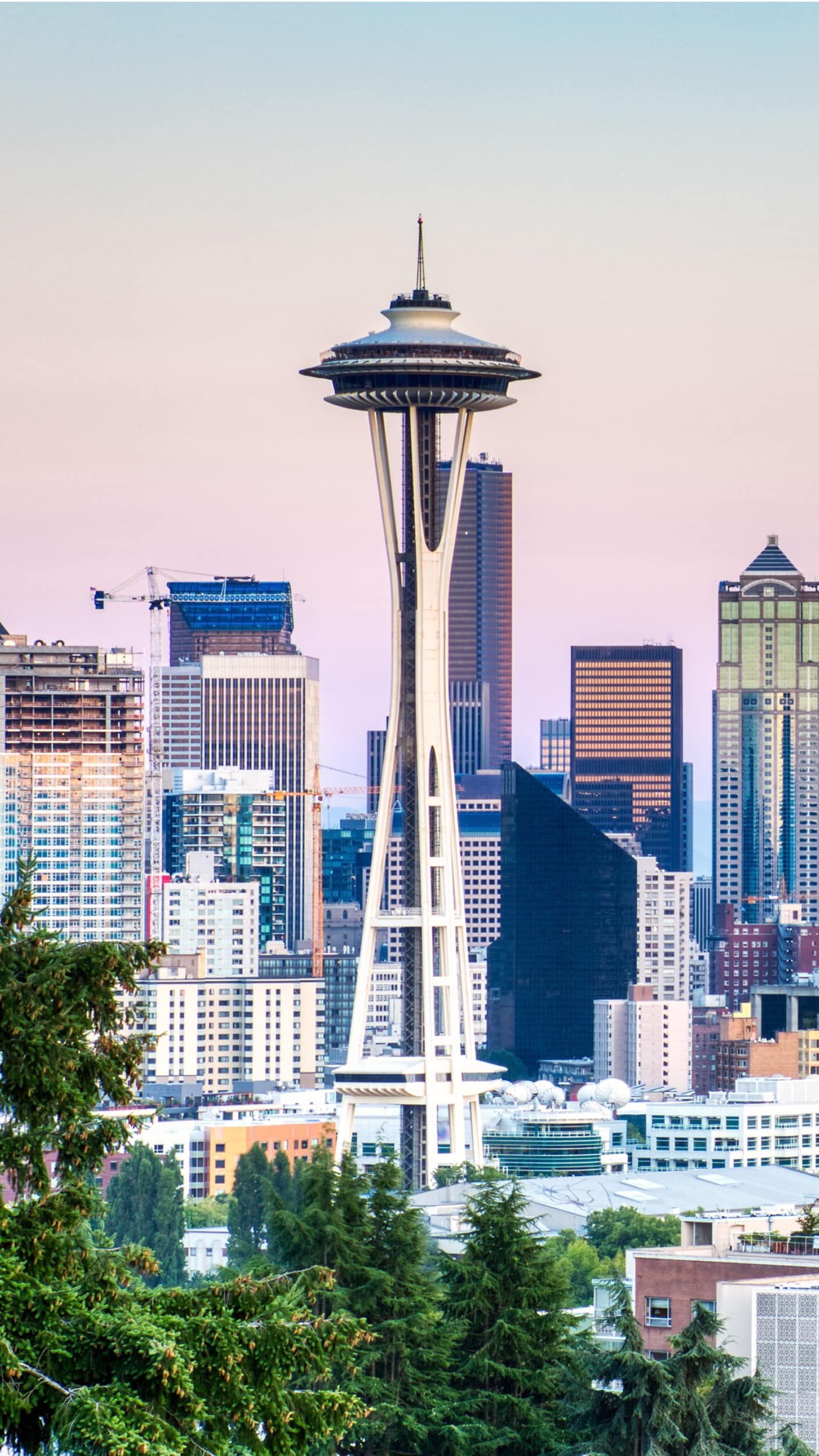 Vertical view of the Seattle Space Needle towering over surrounding downtown skyscrapers at dawn or dusk.