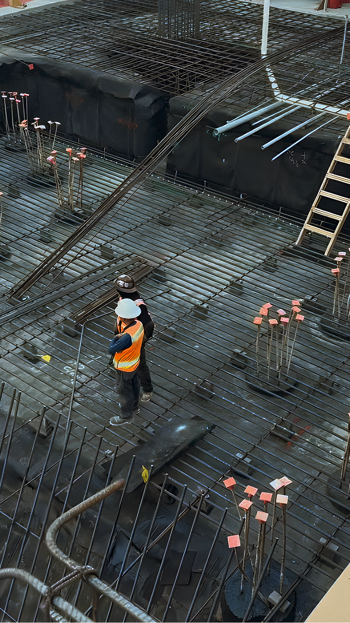 Construction workers standing on a steel rebar grid installed over a Siplast TeraPROOF pre-applied below-grade waterproofing system.