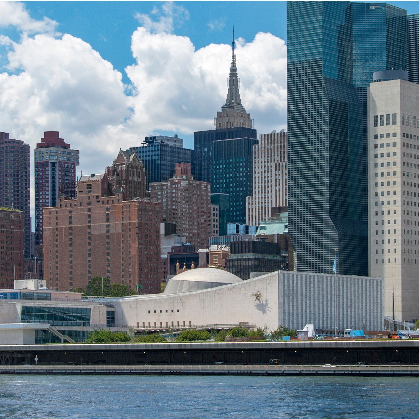 New York City skyline viewed from across the water, featuring the United Nations Headquarters and distant skyscrapers.