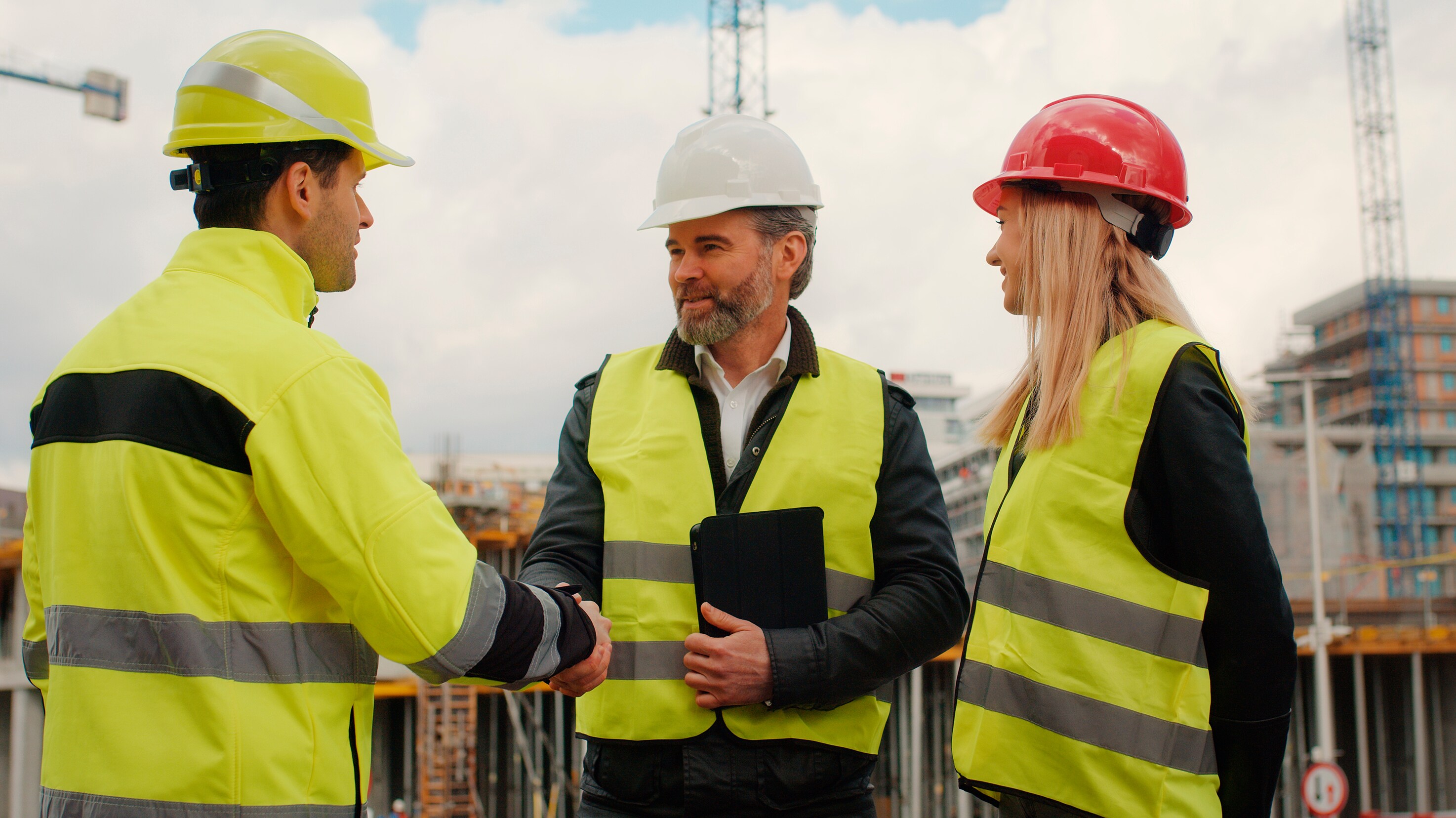 Three construction professionals wearing high-visibility vests and hard hats examining documents at an active construction area