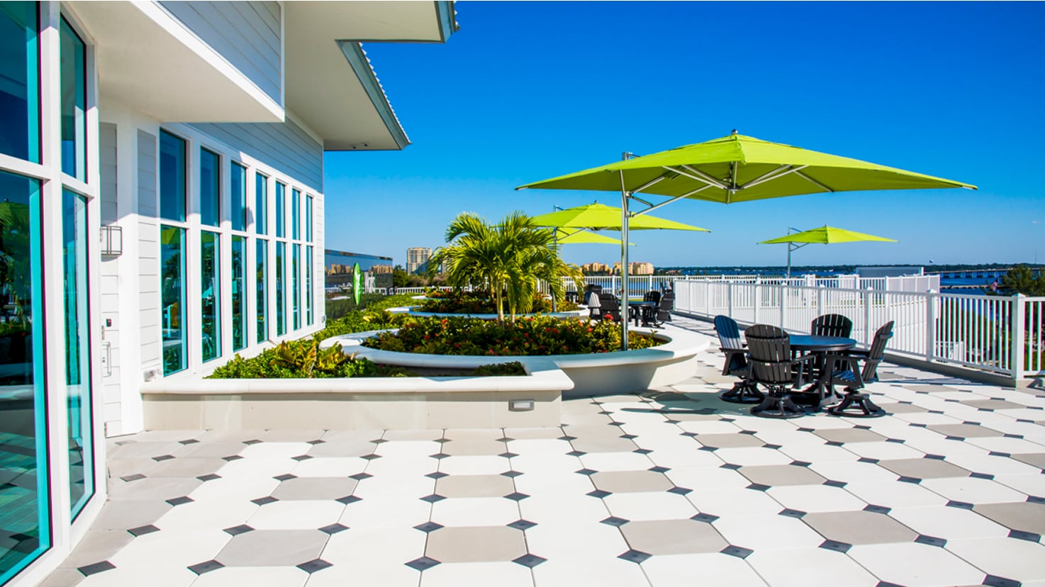 Rooftop patio with geometric tile flooring, raised planter beds, green umbrellas, and outdoor seating on a sunny day
