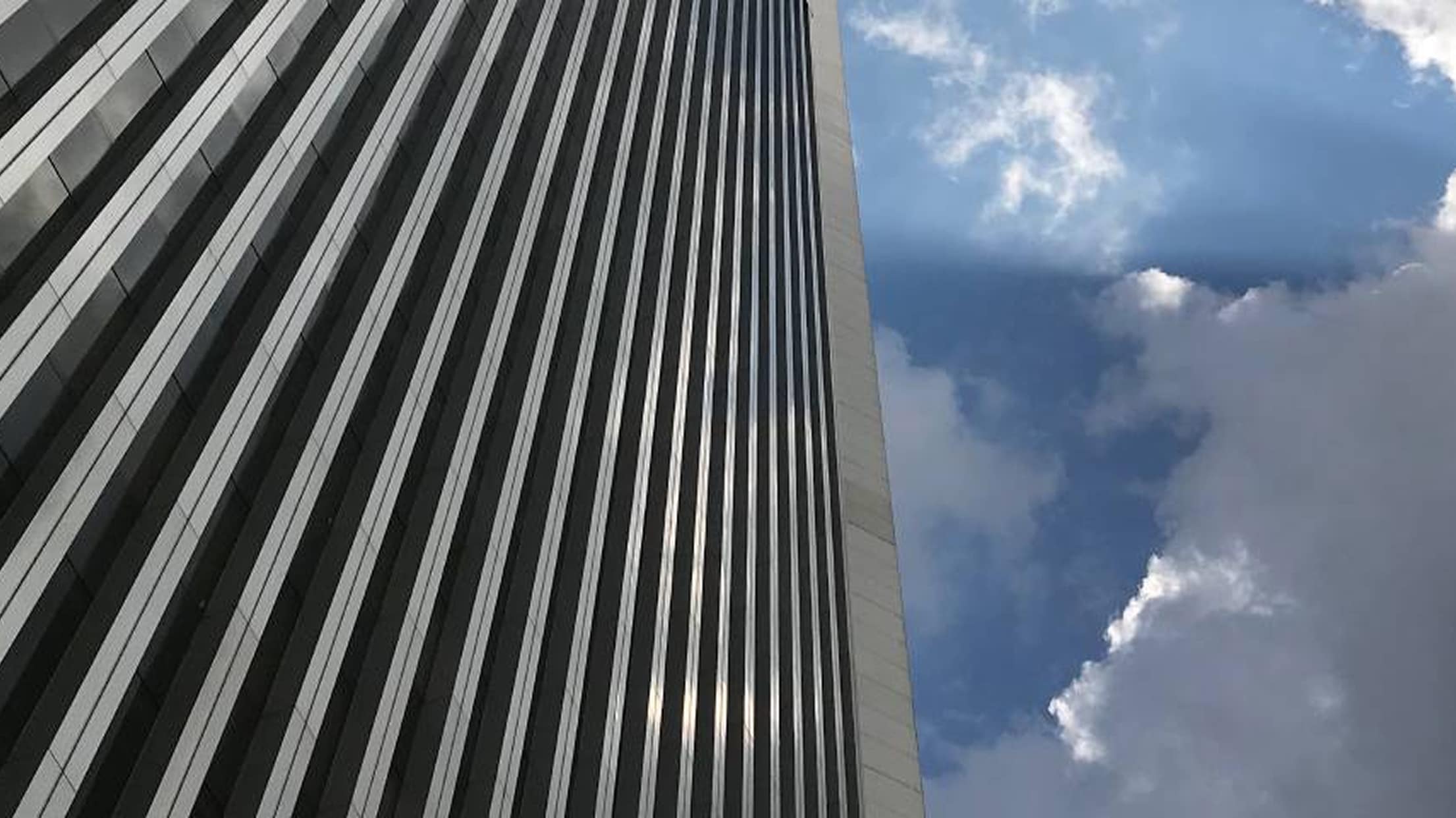 High-rise building with reflective windows under a partly cloudy sky.