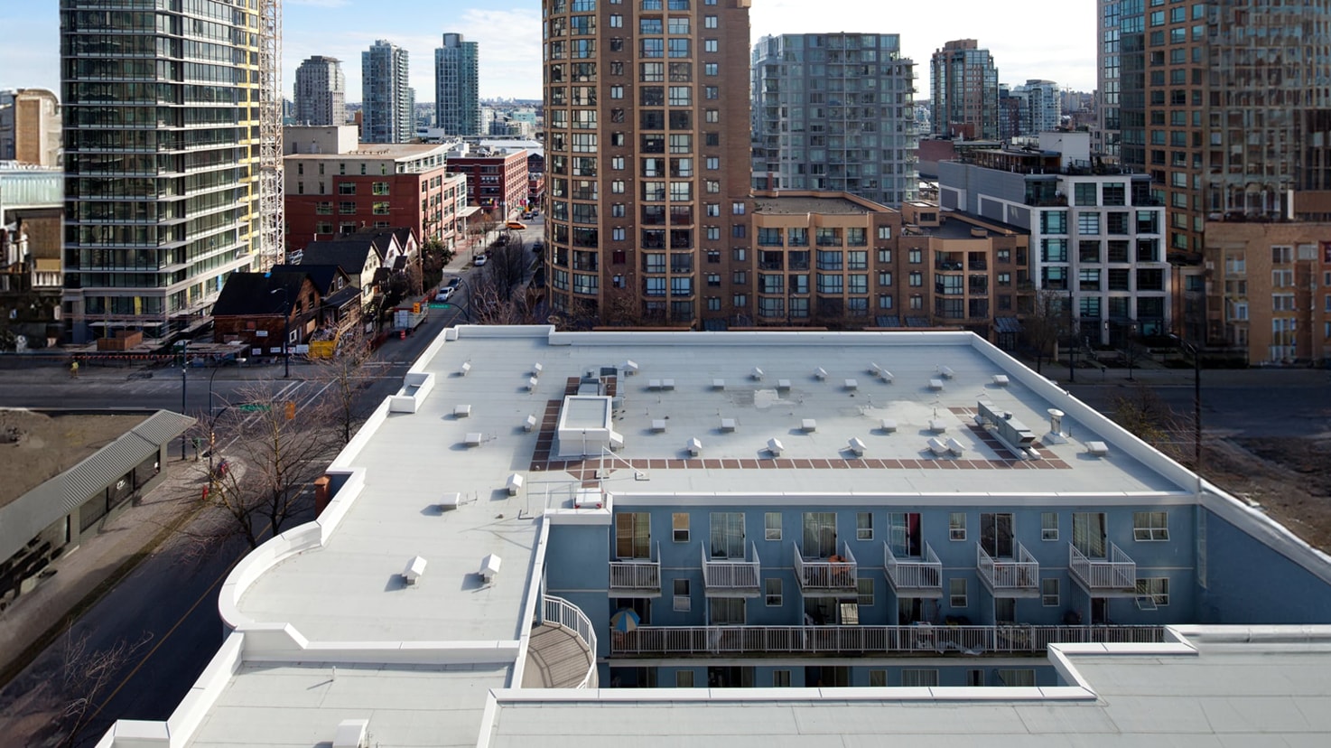 Aerial view of the Jubilee House residential building, showing its light-colored flat roof with SBS membrane and the contrasting facade against the dense urban skyline.