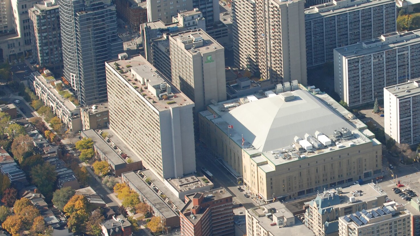 Aerial view of Maple Leaf Gardens in downtown Toronto, showing the large pyramid-shaped roof of the arena surrounded by dense high-rise commercial and residential buildings.